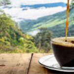 Café sendo despejado na xícara com fundo paisagem natureza